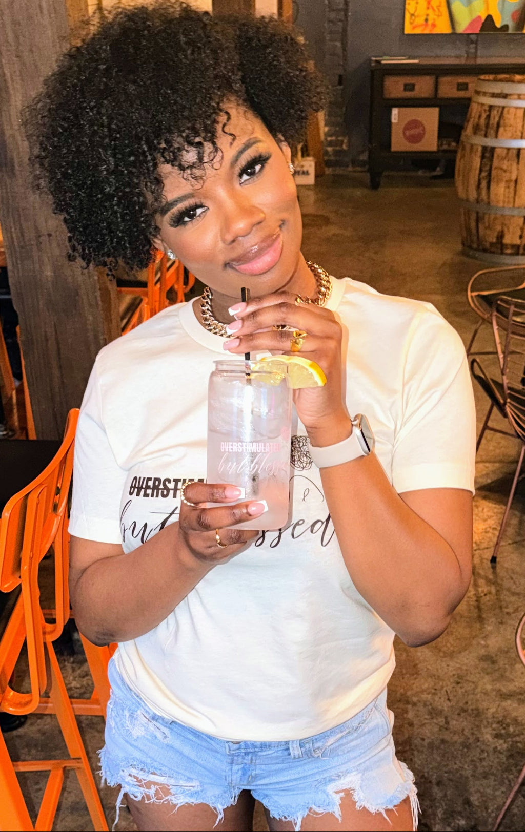 Woman holding a drink in a casual setting with chairs and tables.